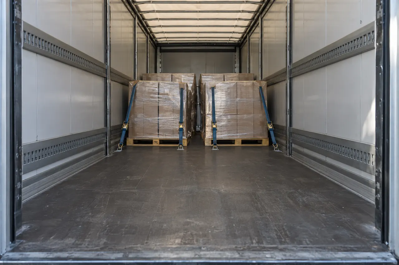 Palets bien trincados en el interior de un tráiler cargado a medias, con luz natural entrando por las puertas.